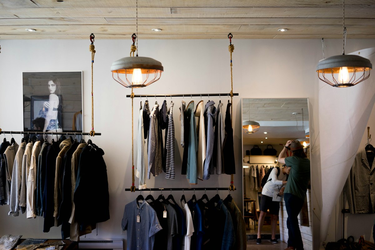Tienda de ropa con paredes blancas, techo de madera y lámparas colgantes.
